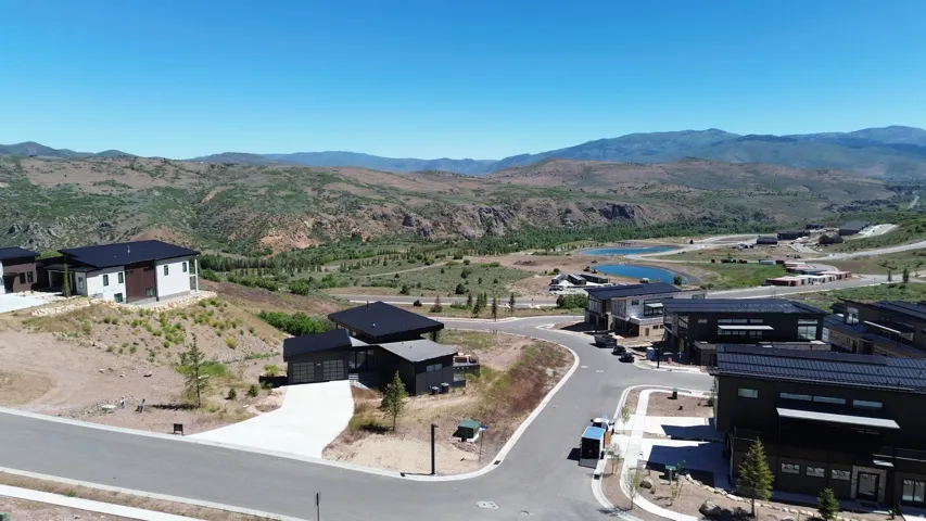 Modern architectural properties on a hillside terrain, featuring a dark roofline, light-toned exterior accents, and expansive mountain scenery