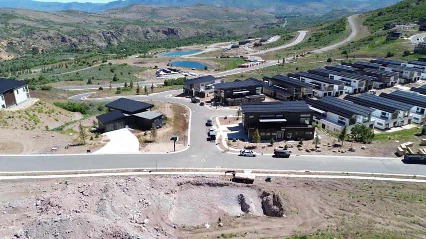 Modern residential development with contemporary architecture, dark-toned facades, multiple detached homes, and paved roadways, situated amidst mountainous terrain with visible water features