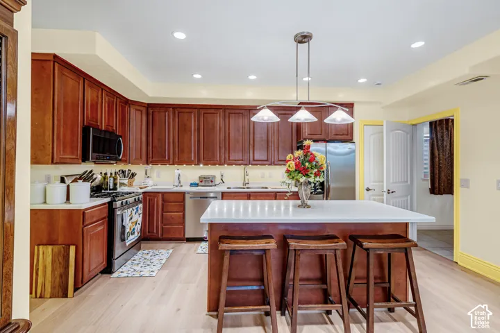 Kitchen featuring wood-finish cabinetry, stainless steel appliances, a center island with a white countertop, and recessed lighting