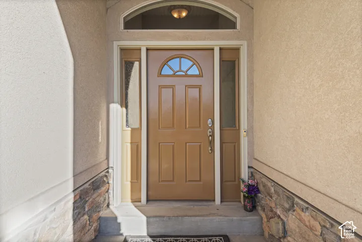 Arched transom window, side light windows, paneled entry door, stucco exterior, and stone veneer accent