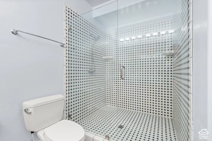Large shower enclosure featuring black and white mosaic tile, a glass door