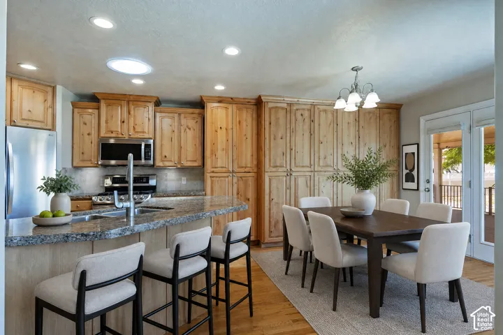 Kitchen and dining area featuring light wood cabinetry, stainless steel appliances, and a granite countertop island with a breakfast bar