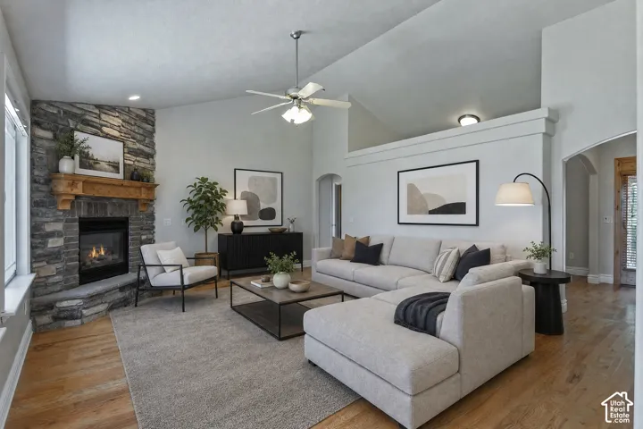 Spacious living area featuring a stone fireplace with a wood mantel, vaulted ceilings, a ceiling fan, wood-finish flooring, and arched doorways