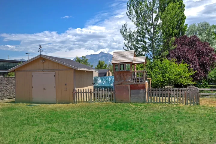 Expansive grassy yard featuring a light-colored storage building with a shingled roof and a weathered picket fence
