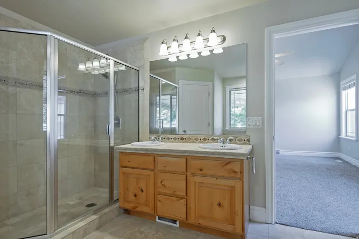 Bathroom featuring a glass-enclosed shower with tile surround, a dual vanity with light wood cabinetry, a large mirror, and overhead sconce lighting