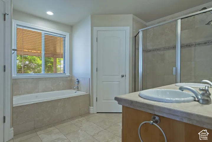 Bathroom featuring a built-in soaking tub with tile surround, a separate glass-enclosed shower with decorative tile inlay, a dual vanity with undermount sinks, and wood-finish cabinetry