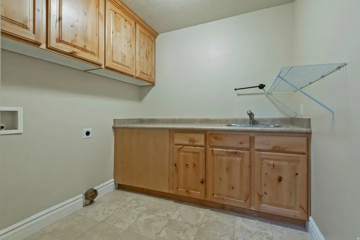 Utility room with wood-finish cabinetry, a built-in sink, and tile flooring