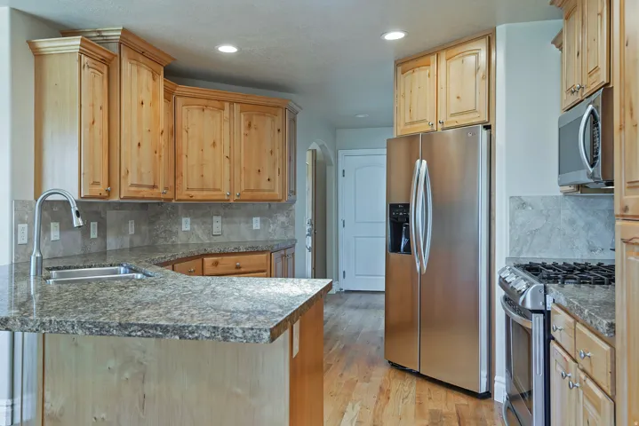 Kitchen featuring light wood cabinetry with crown molding, stone-finish countertops, and a coordinating stone-finish backsplash
