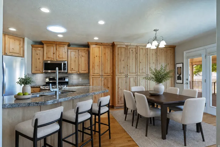 Kitchen and dining area featuring light wood cabinetry, stainless steel appliances, and a granite countertop island with a breakfast bar