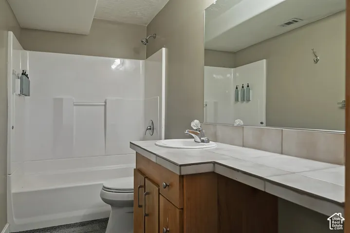 Full bathroom with a white tub/shower combination, a wood-finish vanity, and a tile countertop with an integrated sink