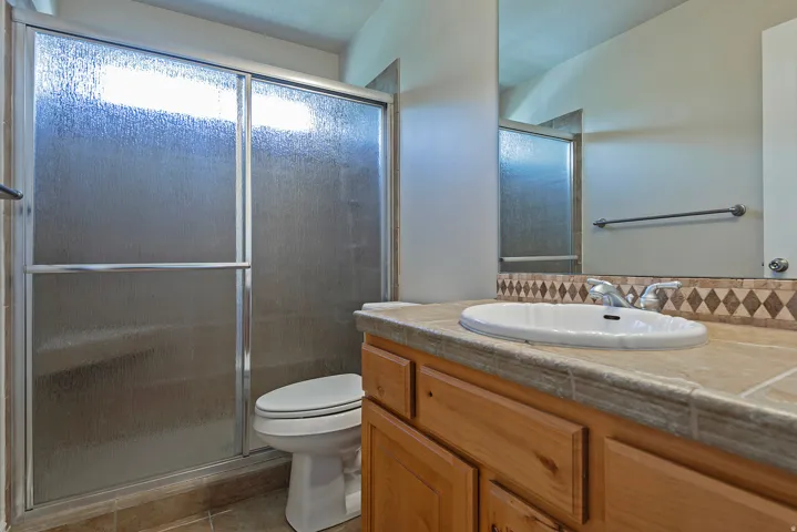 Bathroom featuring a vanity with a drop-in sink, a textured countertop, and a diamond-patterned tile backsplash