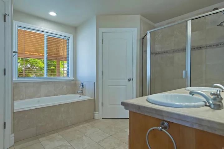 Bathroom featuring a built-in soaking tub with tile surround, a separate glass-enclosed shower with decorative tile inlay, a dual vanity with undermount sinks, and wood-finish cabinetry