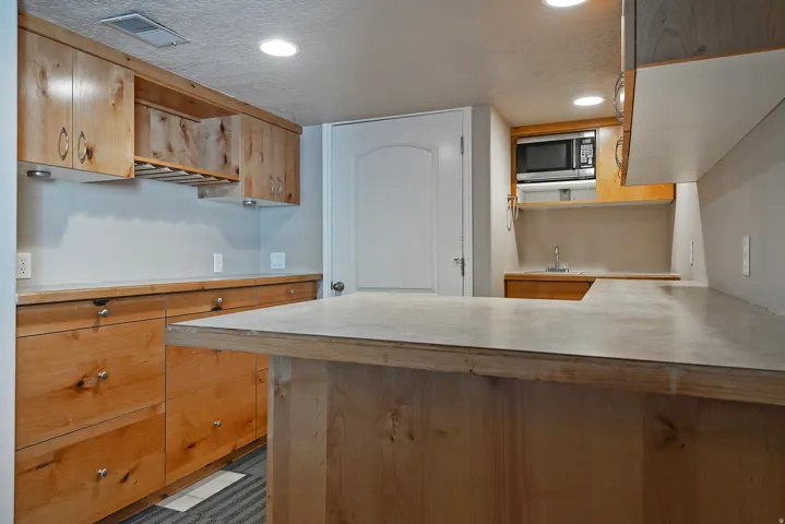 Kitchenette featuring warm wood-finish cabinetry, a built-in microwave, a compact sink, ample countertop space, and recessed lighting