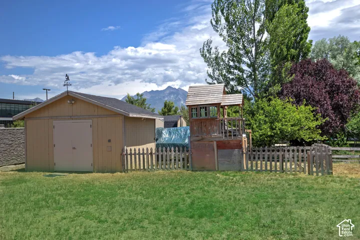 Expansive grassy yard featuring a light-colored storage building with a shingled roof and a weathered picket fence
