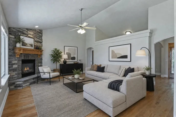Spacious living area featuring a stone fireplace with a wood mantel, vaulted ceilings, a ceiling fan, wood-finish flooring, and arched doorways