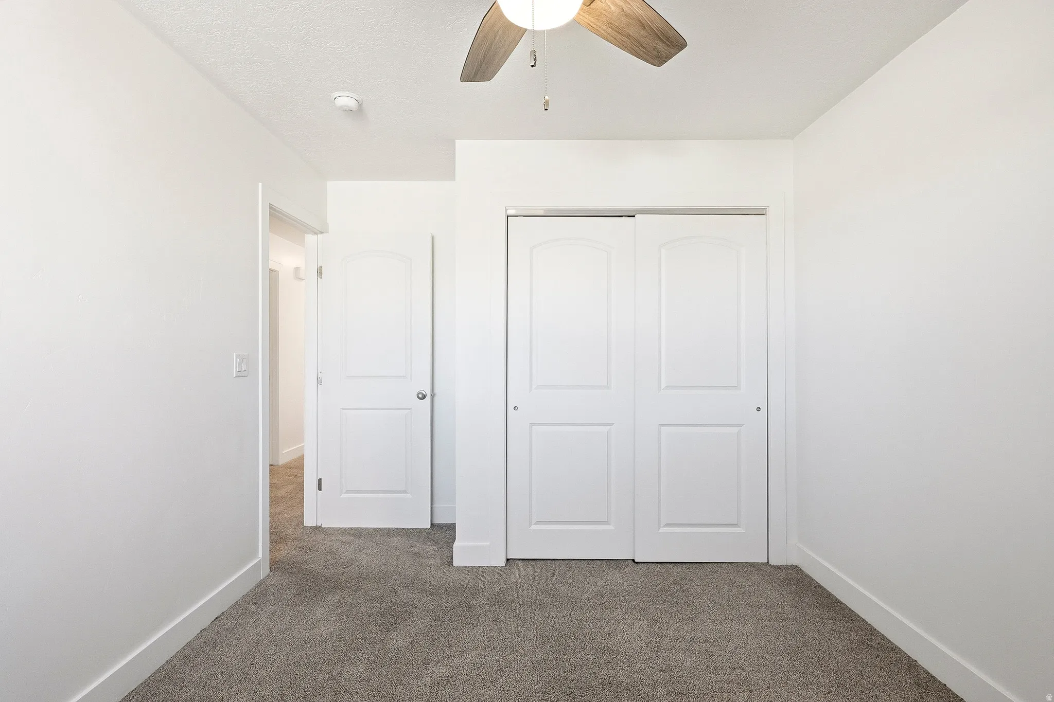 Interior room featuring neutral wall paint, gray carpeting, a ceiling fan with wood-finish blades, white paneled doors, and white baseboards