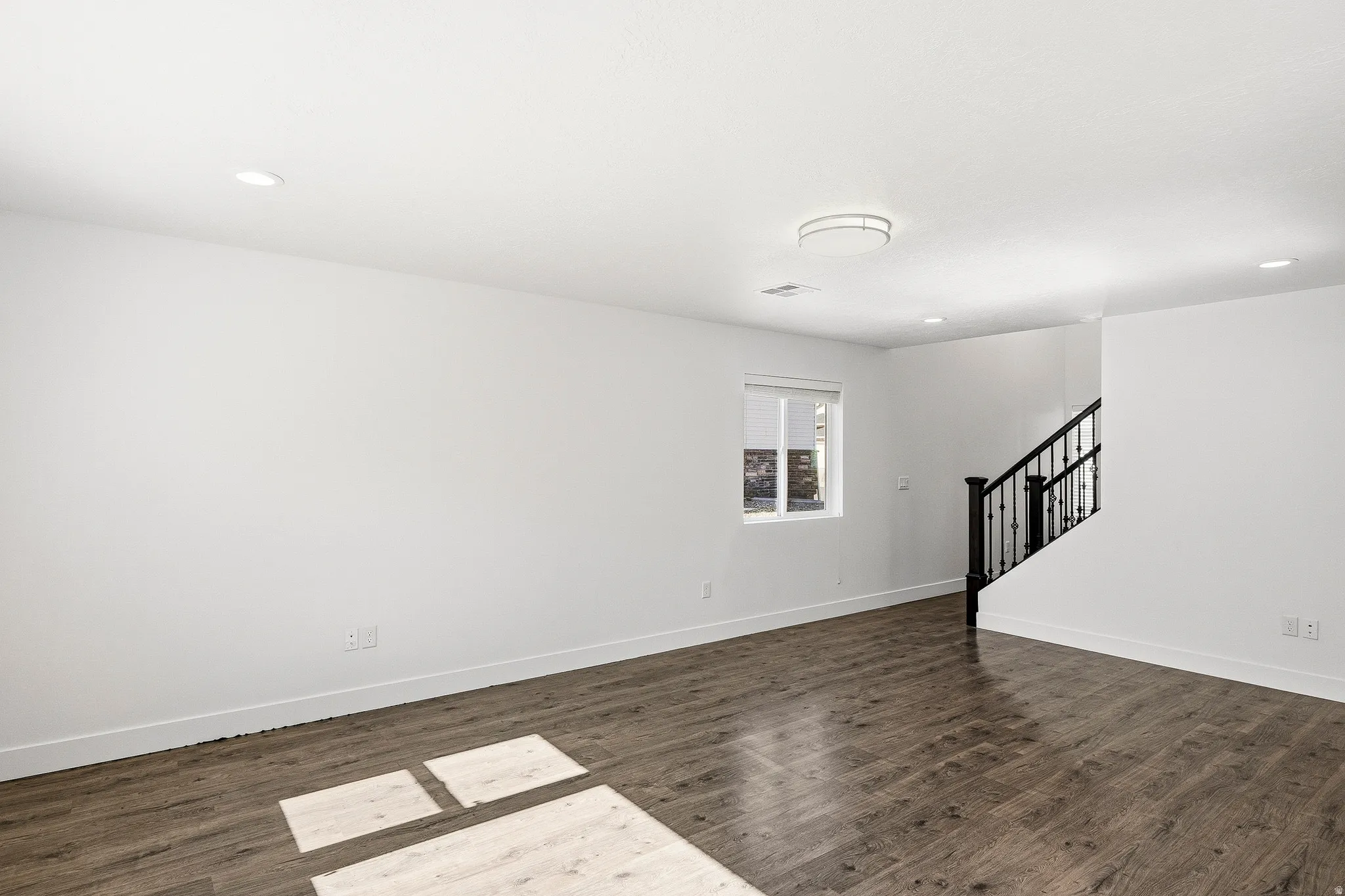 Spacious room featuring wood-finish flooring, recessed lighting, and a contemporary flush-mount ceiling fixture