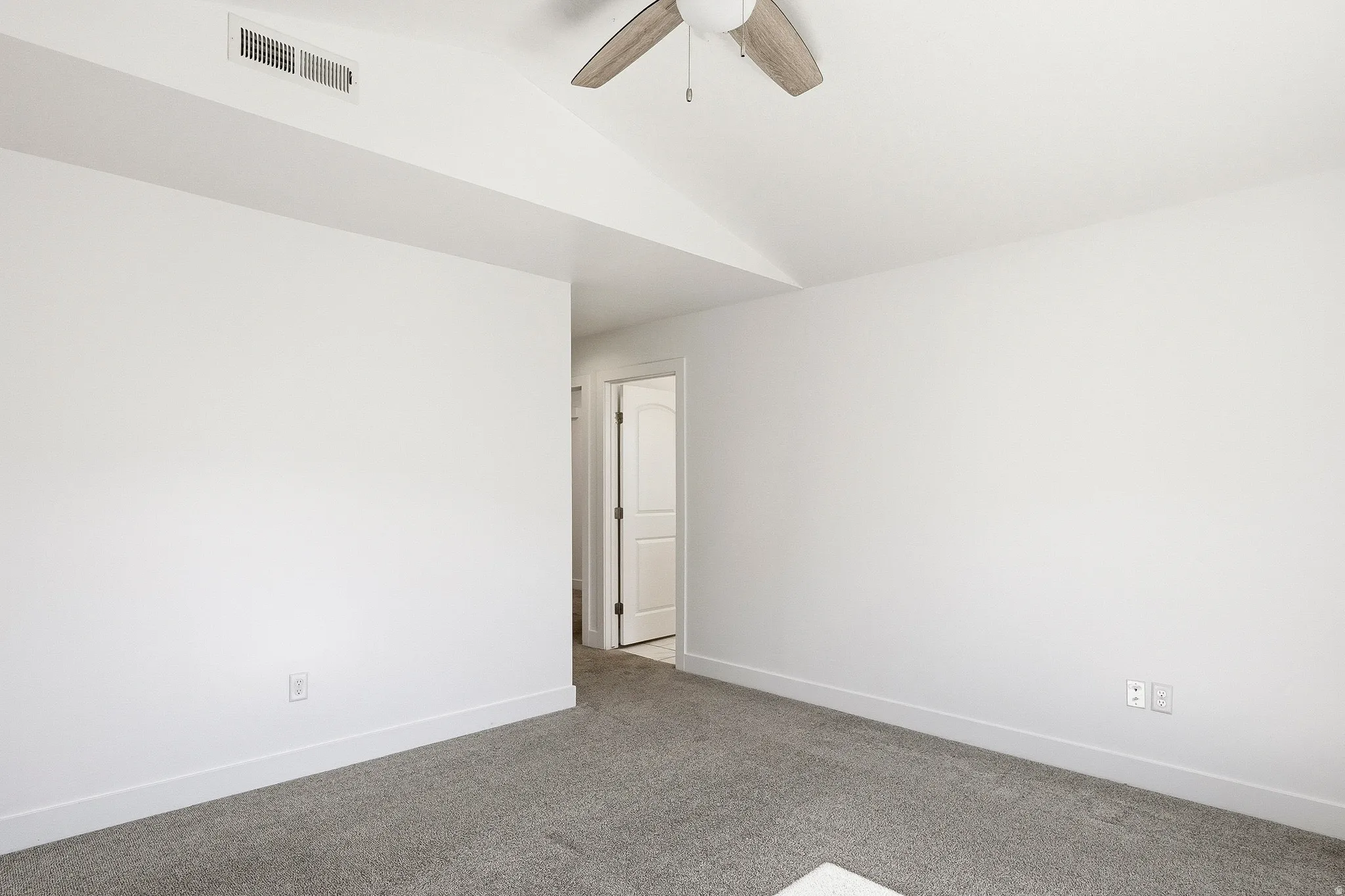 Spacious room featuring neutral carpeting, white walls, and a vaulted ceiling with a ceiling fan