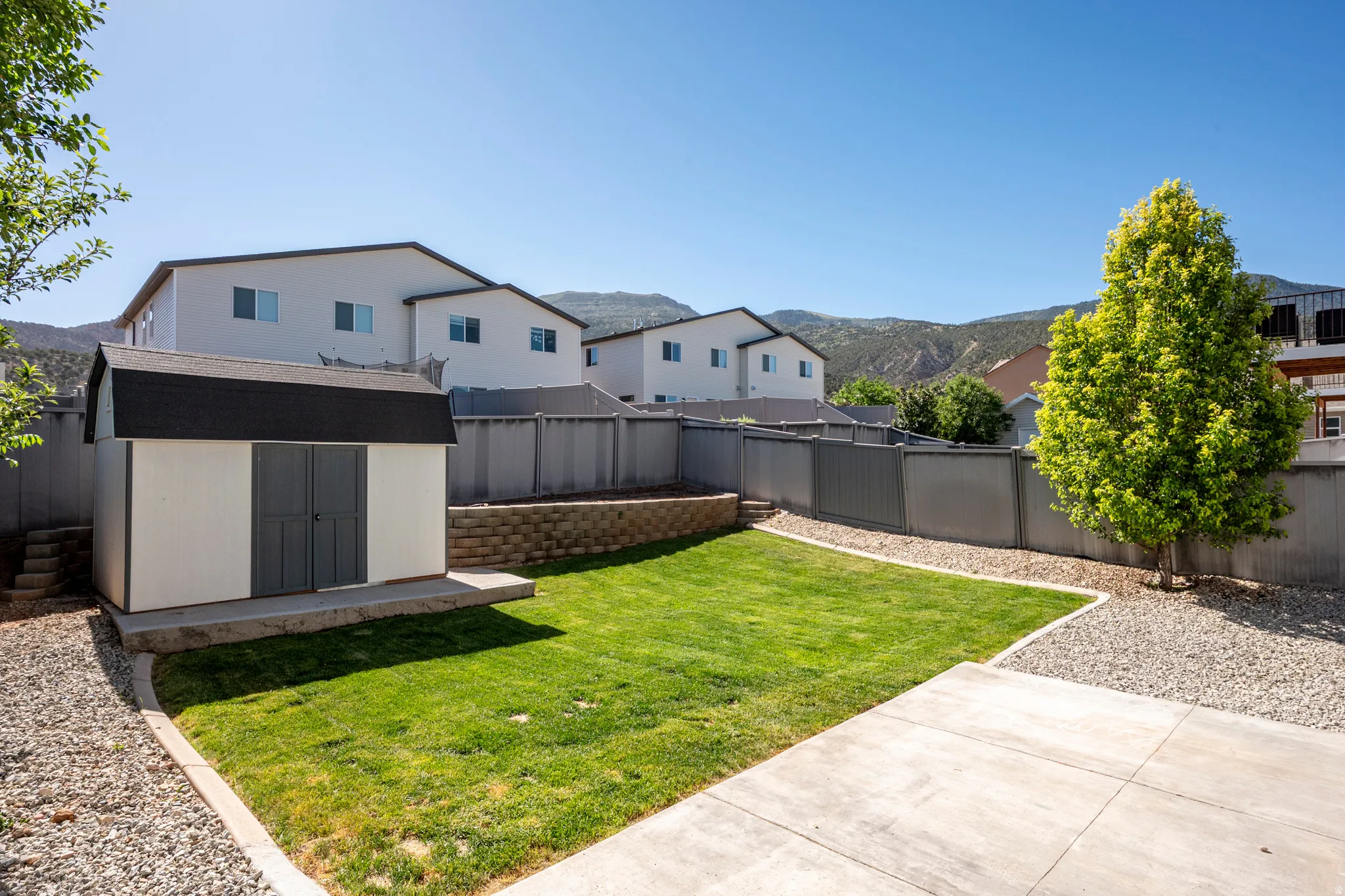 Expansive backyard featuring a green lawn, concrete patio, gravel border, and a freestanding storage shed