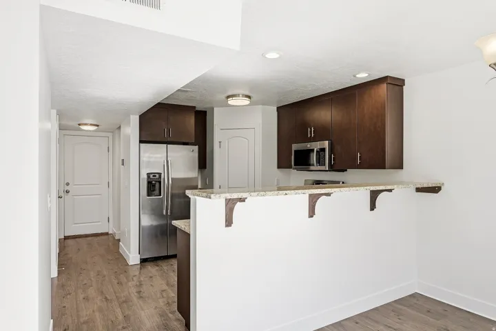 Kitchen area featuring dark wood-finish cabinetry, stainless steel appliances, a breakfast bar with stone-look countertop, and wood-finish flooring