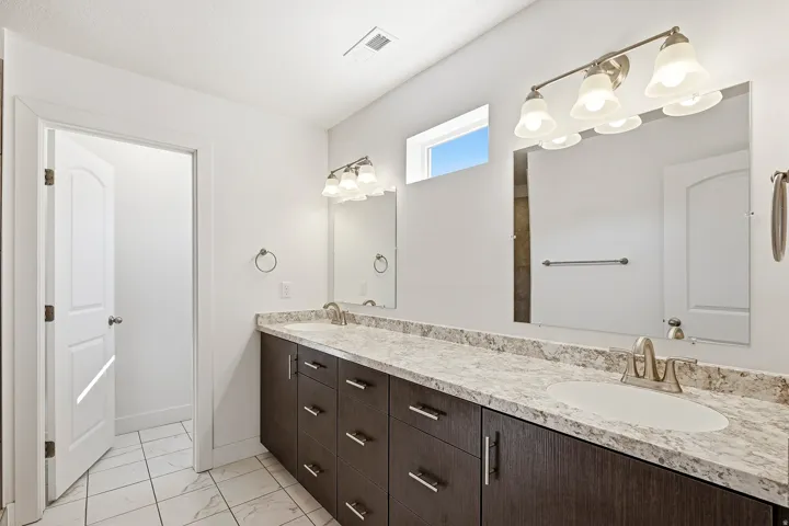 Dual vanity featuring dark wood-finish cabinetry, light speckled countertops, and undermount sinks with brushed nickel fixtures
