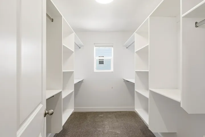 Walk-in closet featuring built-in white shelving, hanging rods, recessed ceiling lighting, and a window with blinds