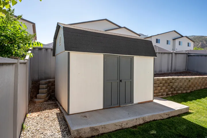 Detached storage shed with a gray shingle roof and double doors