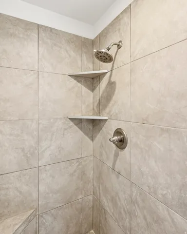 Shower enclosure featuring large format stone-finish wall tiles, a brushed nickel shower head, a coordinating single-handle control, and two built-in corner shelves