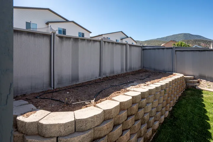 Expansive backyard featuring a tiered landscaping design, a block retaining wall, a dedicated planting area with irrigation lines, green lawn, and a privacy fence