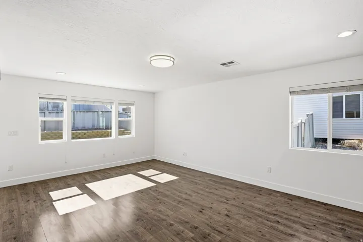 Spacious room featuring wood-finish flooring, white walls, and bright natural light from multiple windows