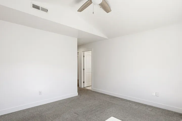Spacious room featuring neutral carpeting, white walls, and a vaulted ceiling with a ceiling fan