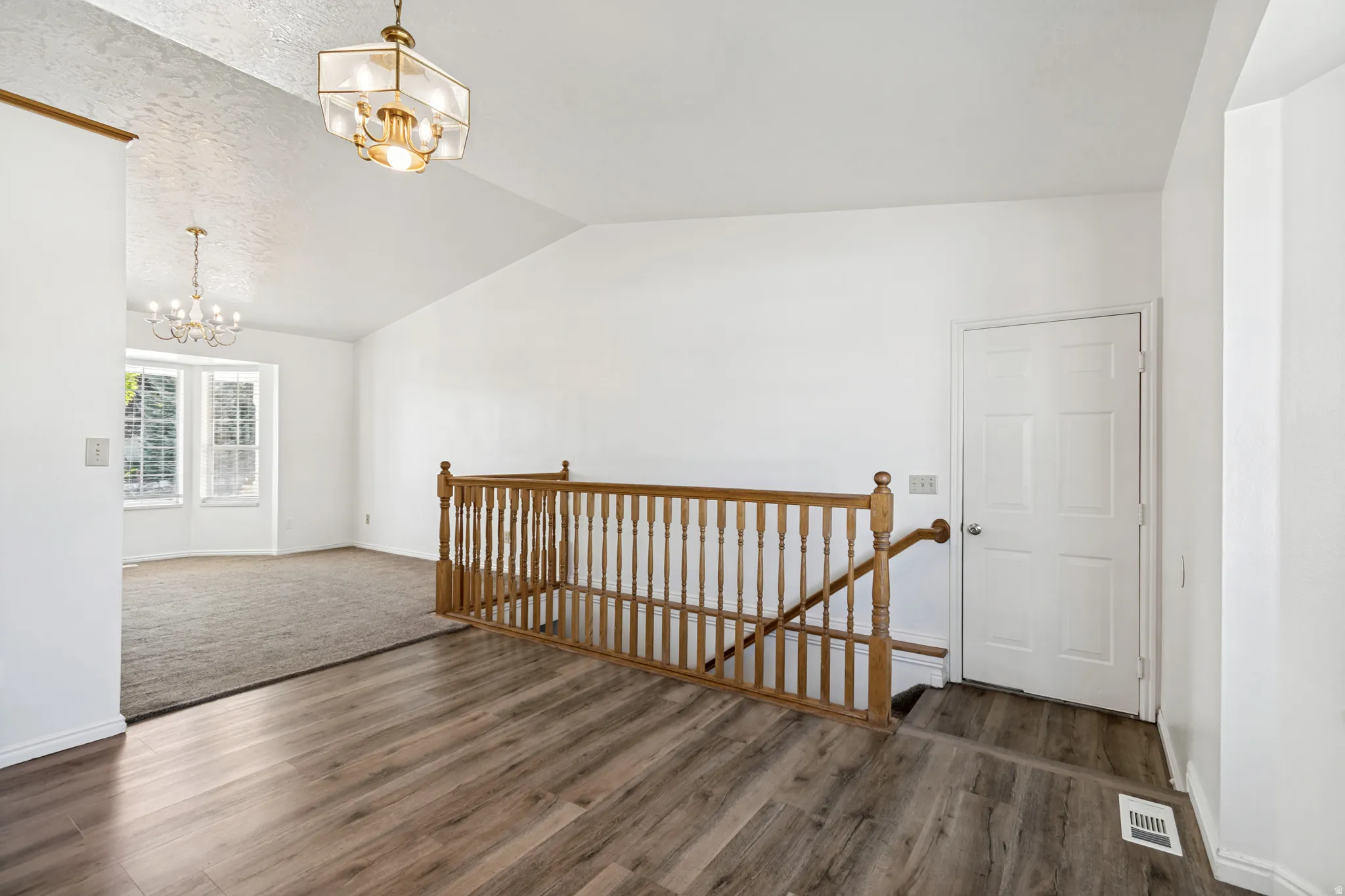Vaulted ceiling with a prominent decorative lighting fixture, wood-finish flooring, and a natural wood staircase railing