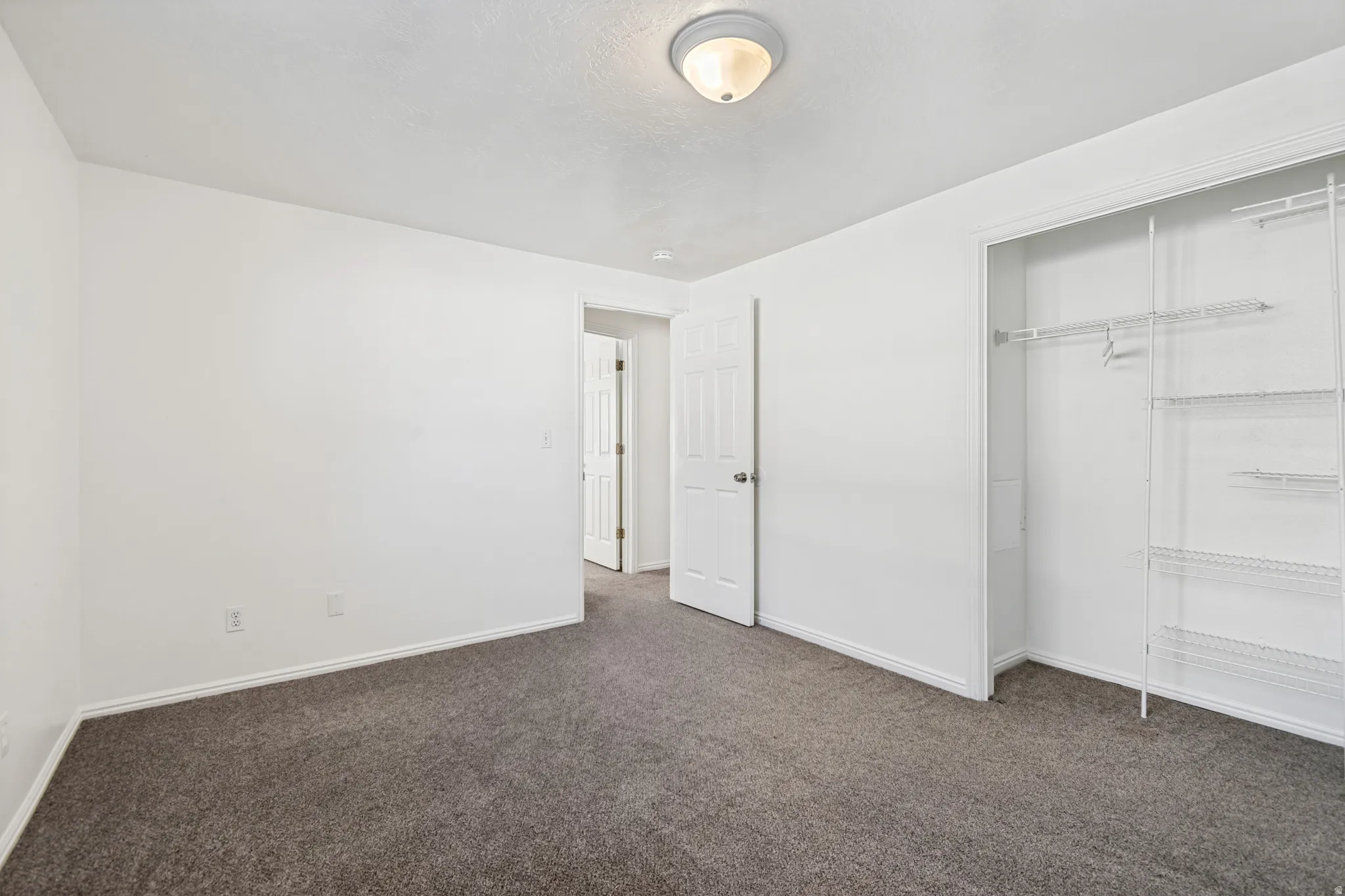 Room featuring plush grey carpeting, bright white walls, a built-in closet with wire shelving, and a flush-mount ceiling light fixture
