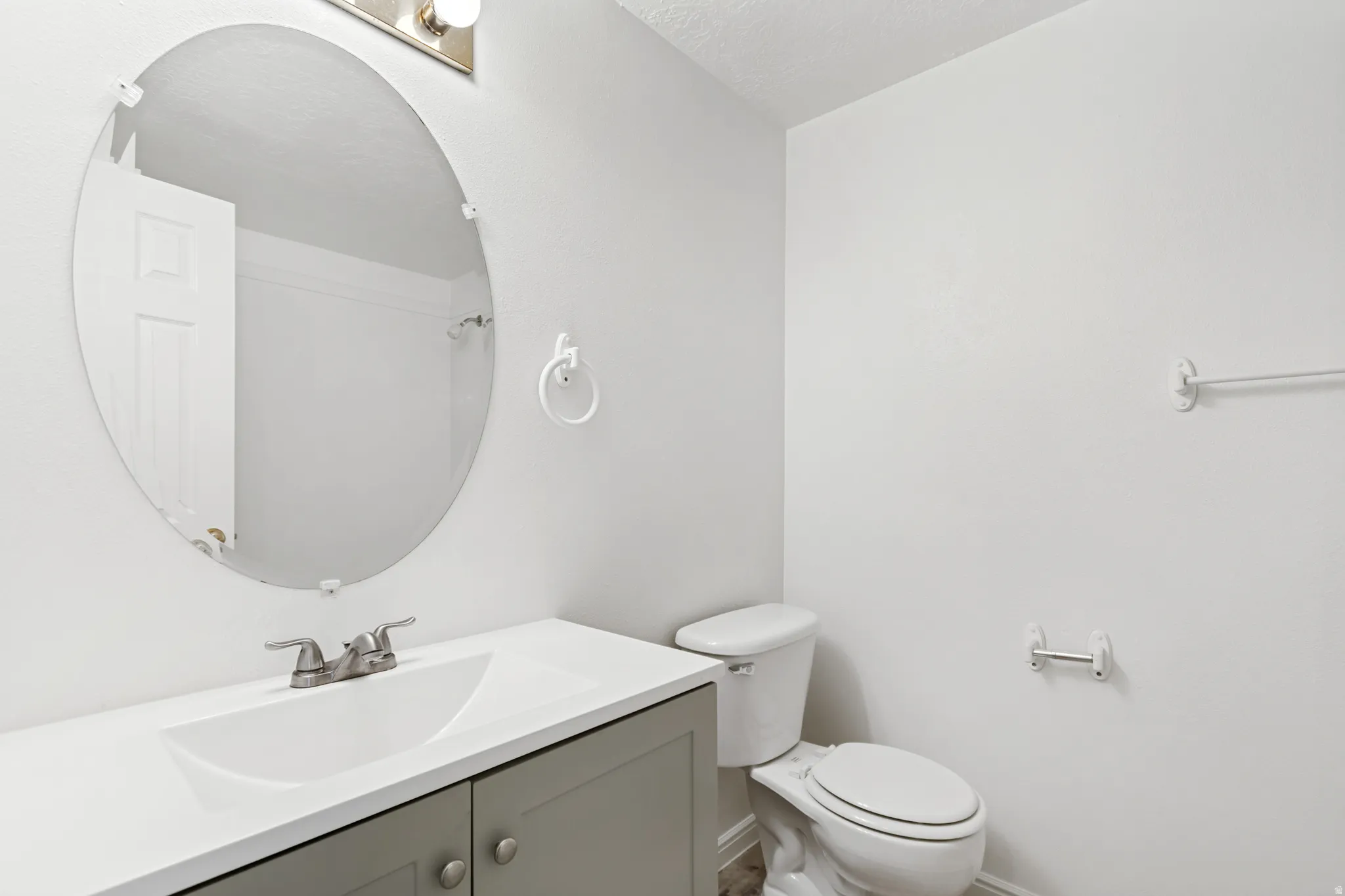 Bathroom featuring a gray vanity with a white countertop and integrated sink, a brushed nickel faucet, an oval mirror, and a white toilet