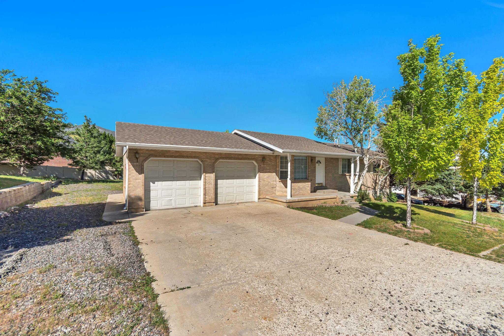 Brick ranch-style residence featuring a two-car garage, a concrete driveway, and a covered front porch with white columns