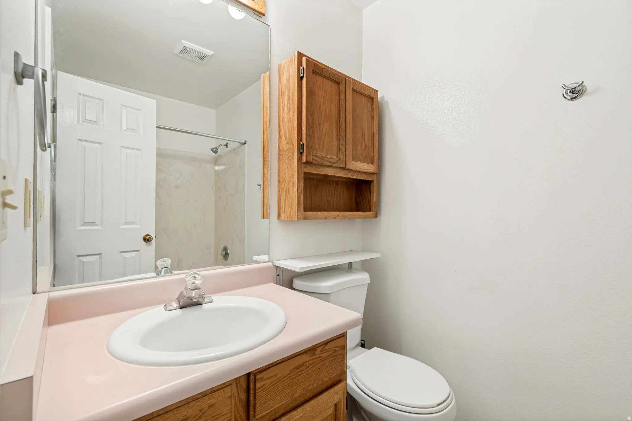 Bathroom vanity featuring a pink countertop with an integrated sink, wood-finish cabinetry, and a mirrored wall