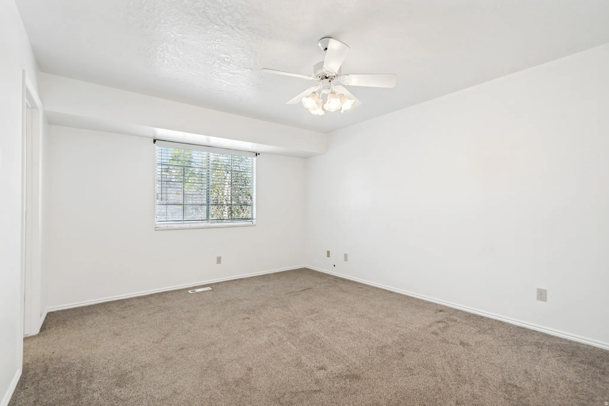 Spacious room featuring neutral carpeting, a ceiling fan with integrated lighting, and a window with blinds
