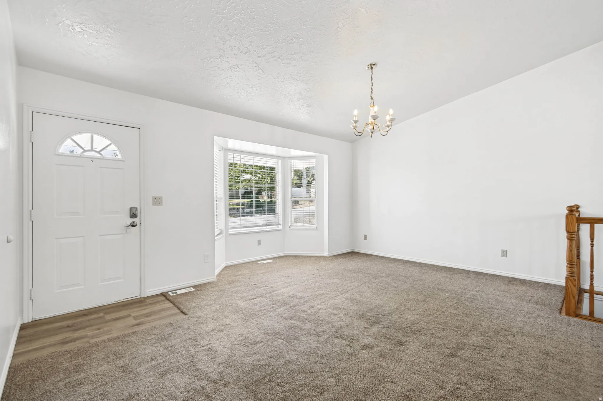 Living area featuring a bay window, chandelier lighting, wood-finish flooring at the entry, and carpet throughout