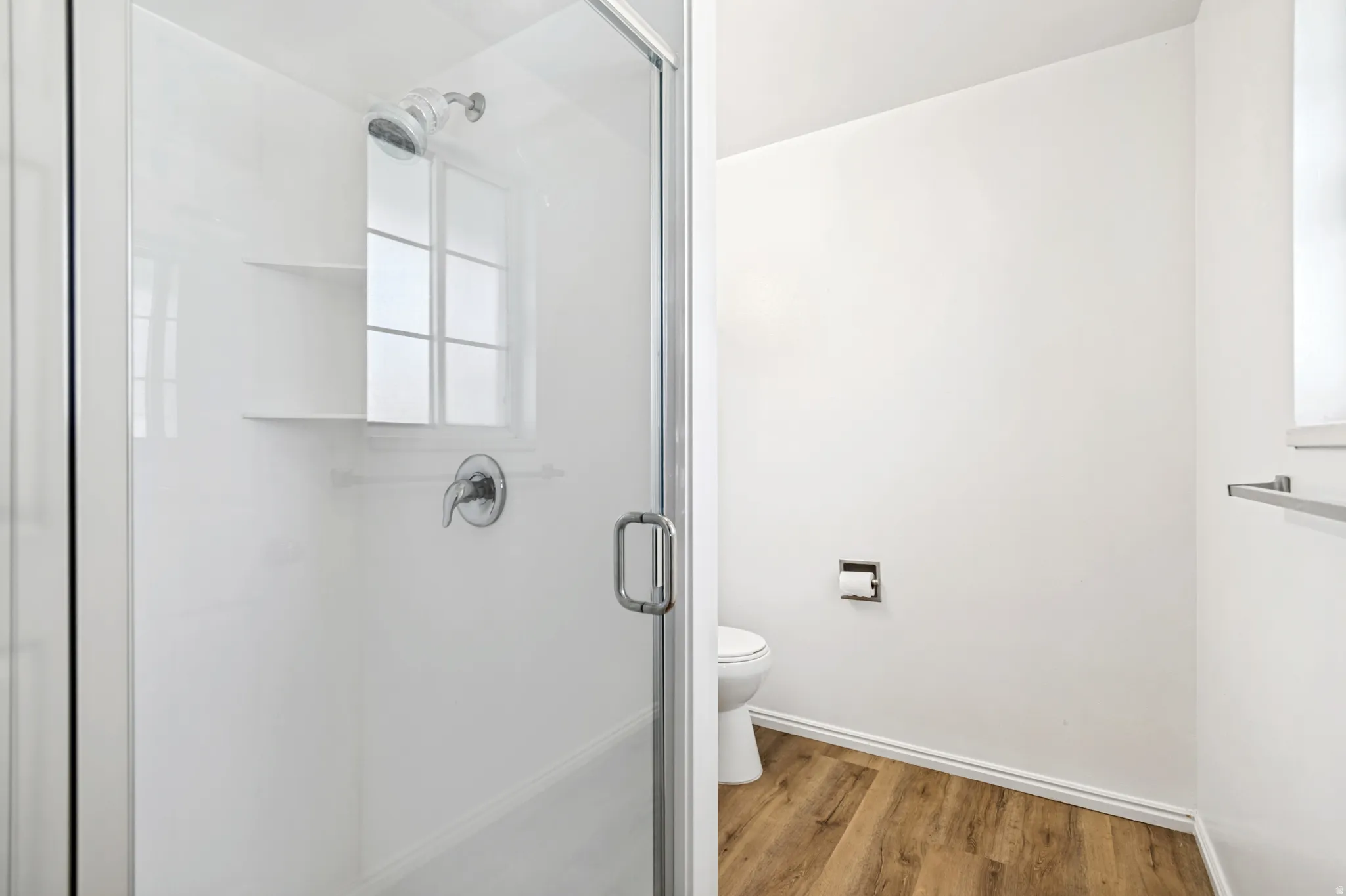 White shower enclosure with a clear glass door, chrome fixtures, and built-in shelving
