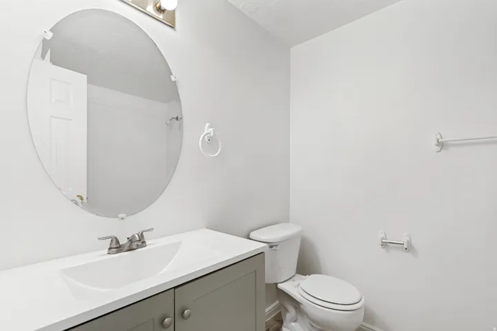 Bathroom featuring a gray vanity with a white countertop and integrated sink, a brushed nickel faucet, an oval mirror, and a white toilet