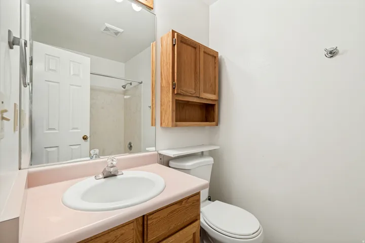 Bathroom vanity featuring a pink countertop with an integrated sink, wood-finish cabinetry, and a mirrored wall