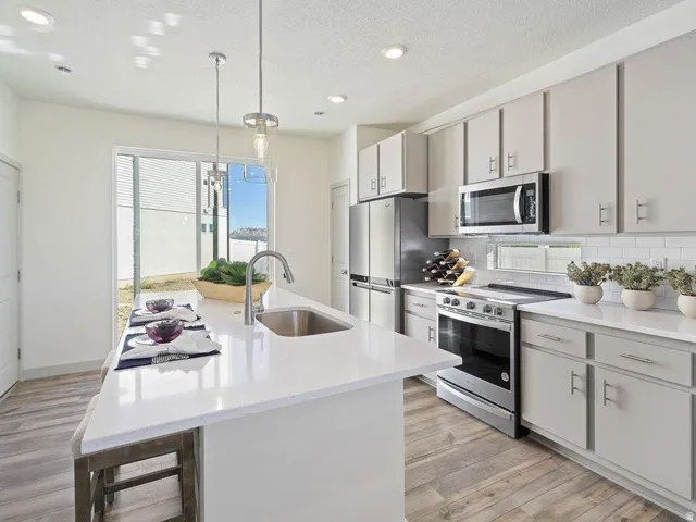 Modern kitchen featuring a large central island with seating, stainless steel appliances, light cabinetry, white countertops, and wood-finish flooring