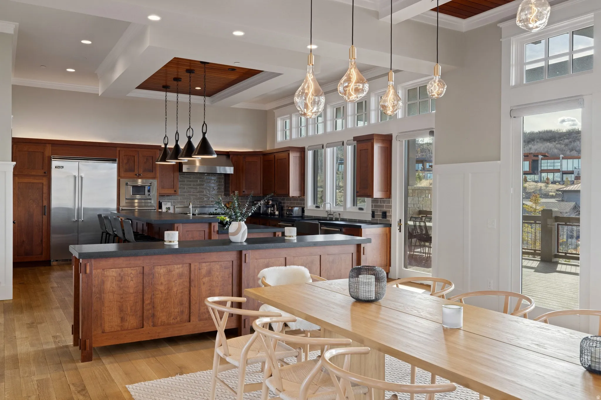 Gourmet kitchen and dining area featuring premium wood-finish flooring, a large kitchen island with dark countertops, wood cabinetry, and stainless steel appliances