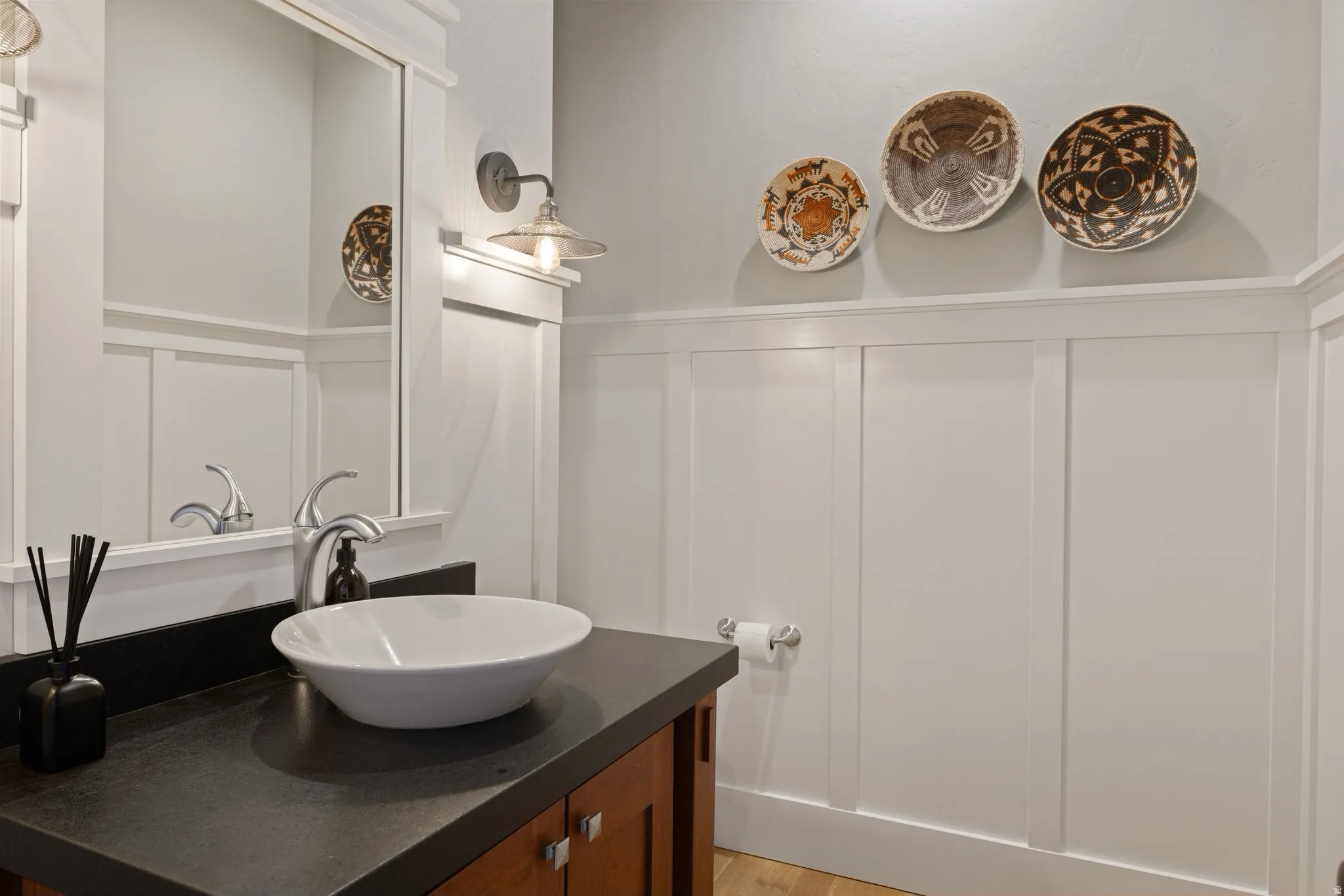 Powder room featuring board and batten wainscoting, wood vanity with dark countertop, vessel sink, and wall-mounted light fixture