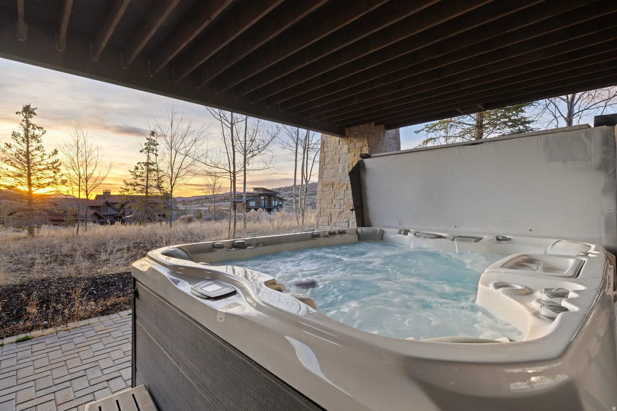 Outdoor hot tub under a covered patio with exposed wood ceiling beams