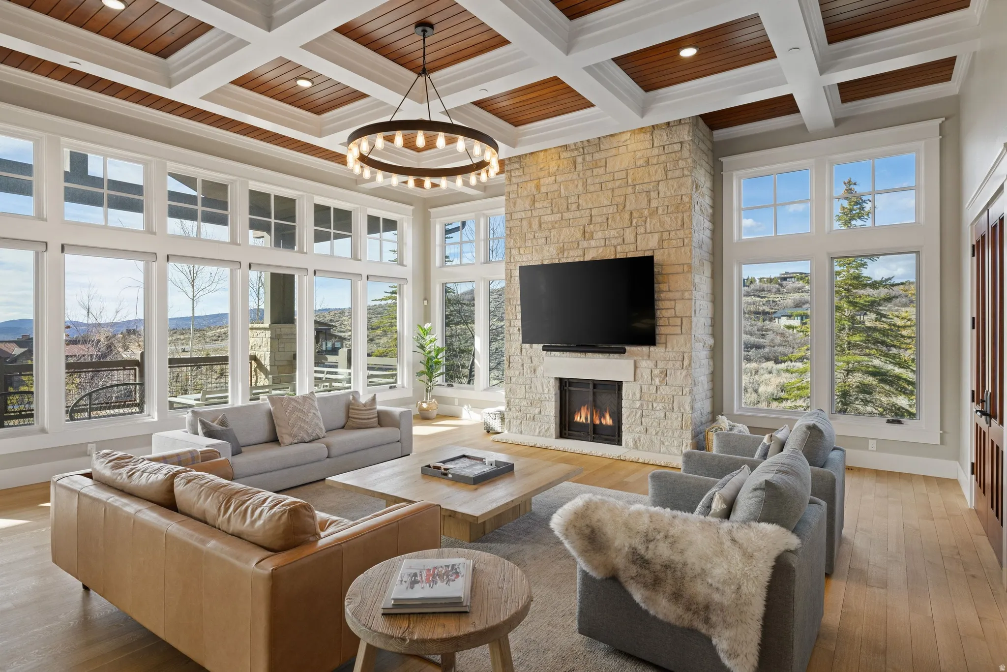 Spacious living area featuring a coffered ceiling with wood-finish panels, a stone-clad fireplace, and extensive window walls
