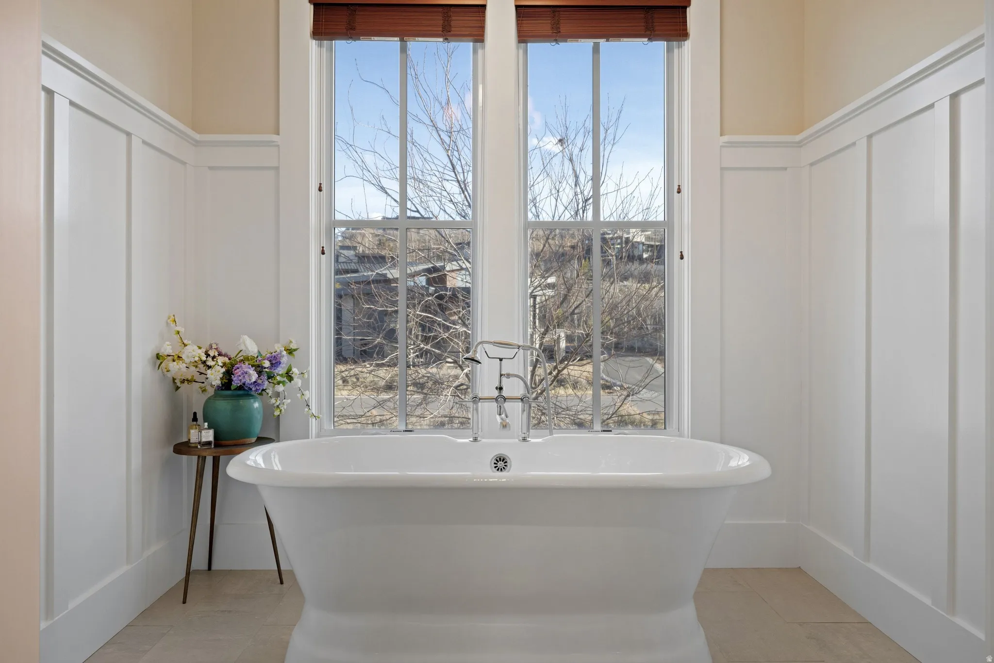 Freestanding soaking tub with a floor-mounted polished chrome faucet, set against a backdrop of two tall windows