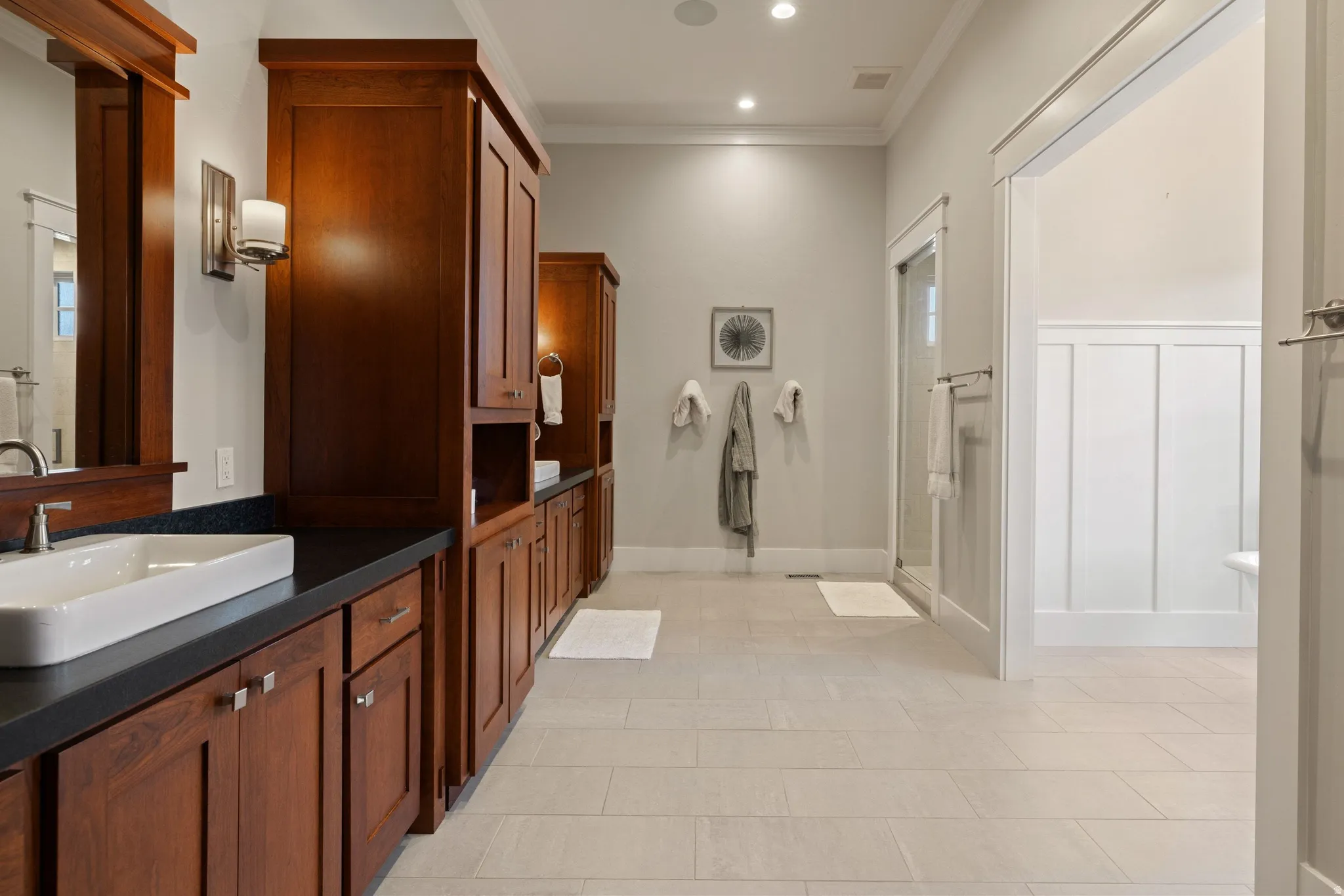 Spacious bathroom featuring extensive wood cabinetry, dark countertops, and dual vessel sinks