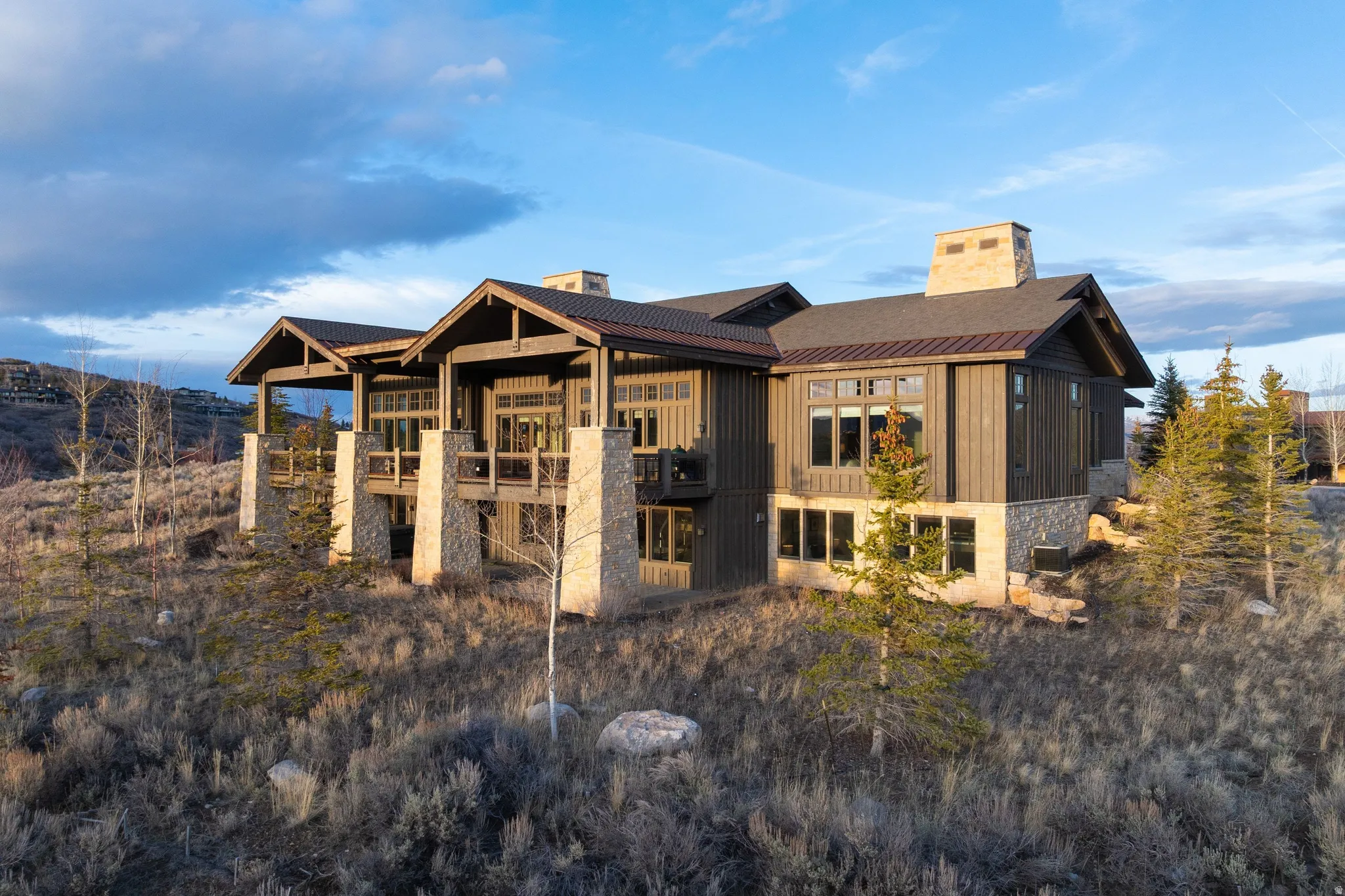 Modern mountain-style residence featuring a prominent stone base, dark vertical siding, and multiple balconies with dark railings