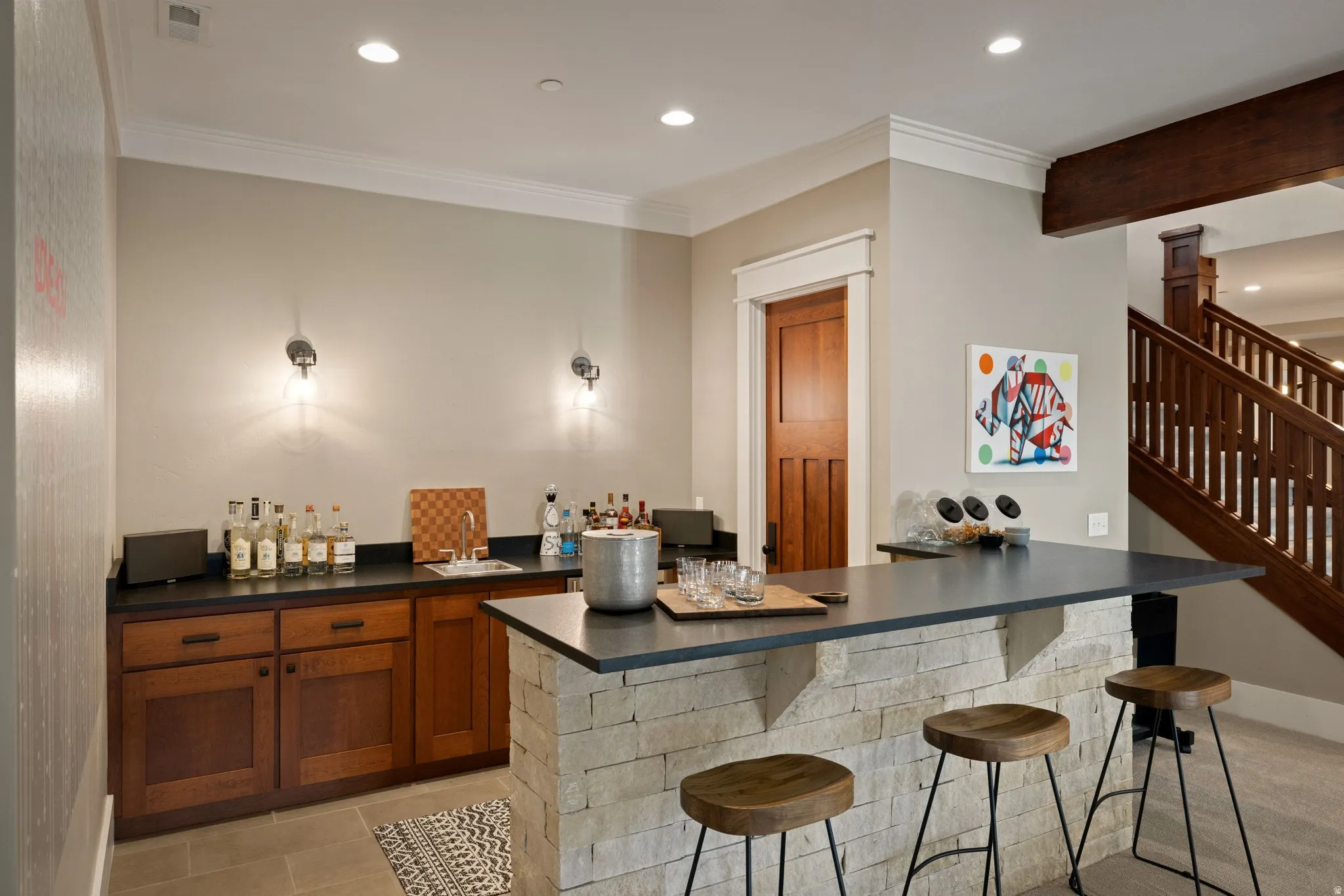 Entertainment area featuring a stone-clad bar with a dark countertop, recessed lighting, and built-in wood cabinetry with a sink